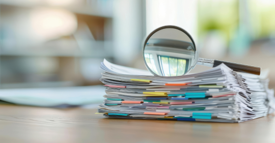 stack of documents with binder clips and a magnifying glass sitting on top of the stack Audit, Review, or Compilation: Which Assurance Service Does Your Business Need cjg partners