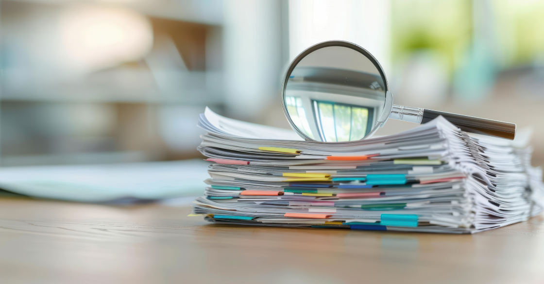 stack of papers with a magnifying glass sitting on top Audit Review Compilation Assurance