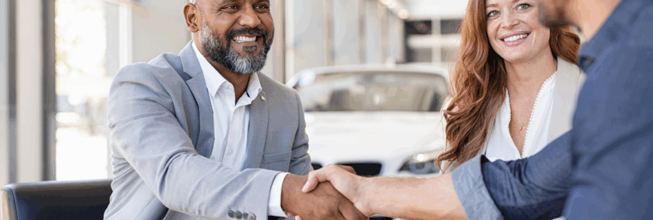 two men shaking hands across a table with papers and a woman smiling in the background the hidden risks of not having a buy-sell agreement
