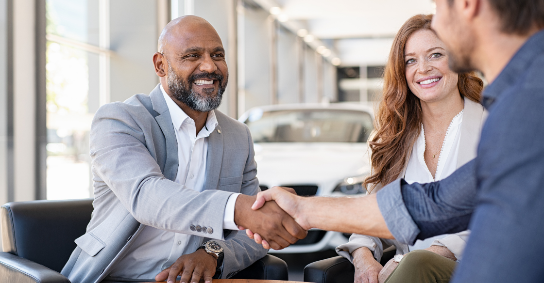 two men shaking hands across a table with papers and a woman smiling in the background the hidden risks of not having a buy-sell agreement