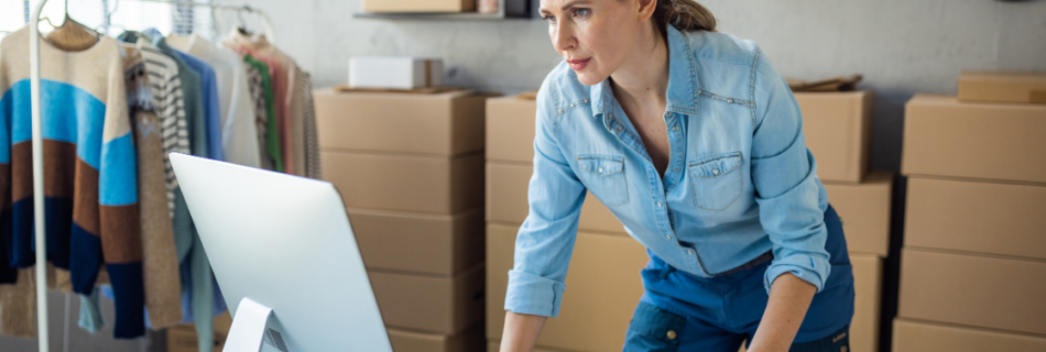 woman standing at a desk and looking at a computer with boxes in the background and clothes hanging on a rack reasonable compensation cjg partners accounting schaumburg