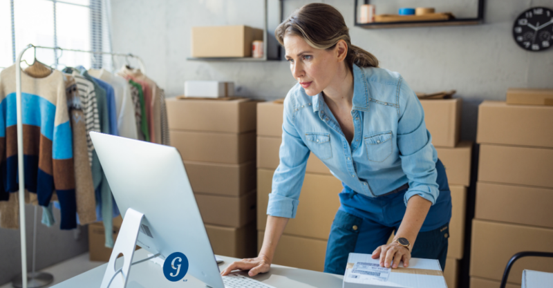 woman standing at a desk and looking at a computer with boxes in the background and clothes hanging on a rack reasonable compensation cjg partners accounting schaumburg