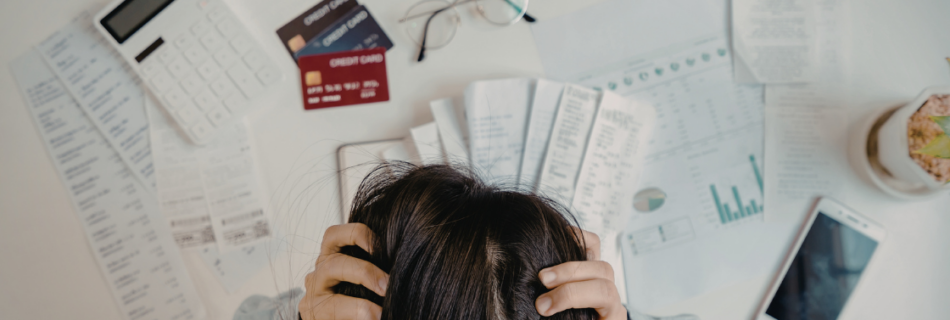 woman with her hands in her hair leaning over a pile of credit cards and paperwork looking frustrated 4 Bookkeeping Mistakes That Are Costing Your Business More Than You Think cjgpartners