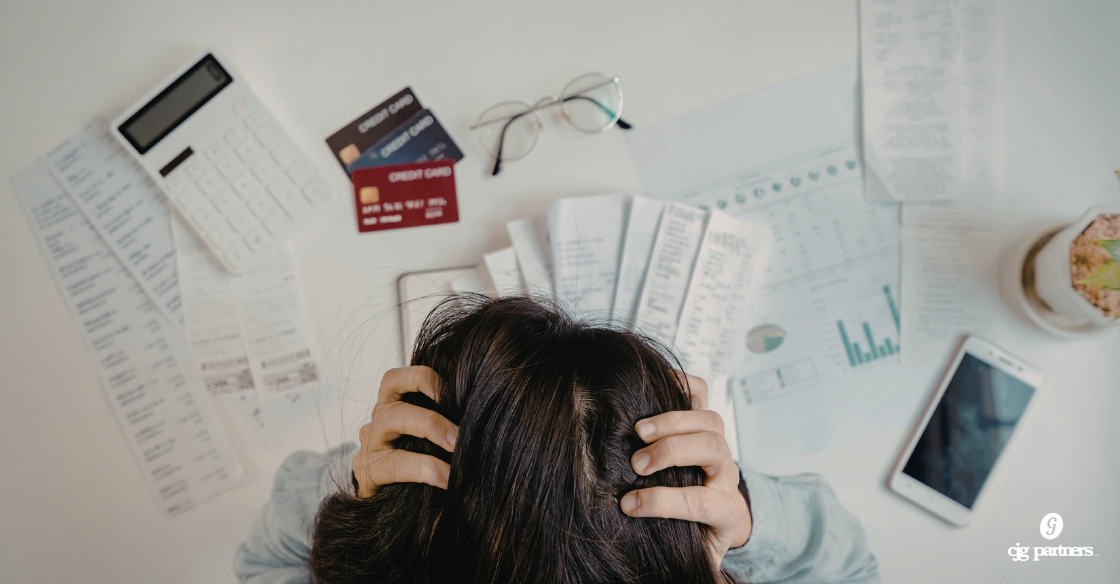 woman with her hands in her hair leaning over a pile of credit cards and paperwork looking frustrated 4 Bookkeeping Mistakes That Are Costing Your Business More Than You Think cjgpartners