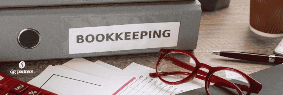 binders with bookkeeping on the spine and papers, glasses, and a calculator on a table The Unexpected Value in Consistent Bookkeeping cjg partners